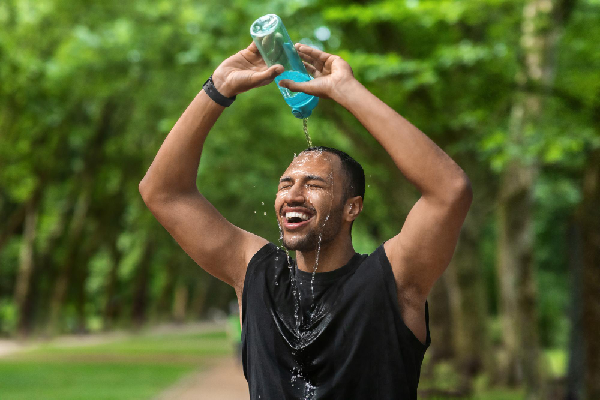 blije sportende man sproeit water uit fles over zijn hoofd